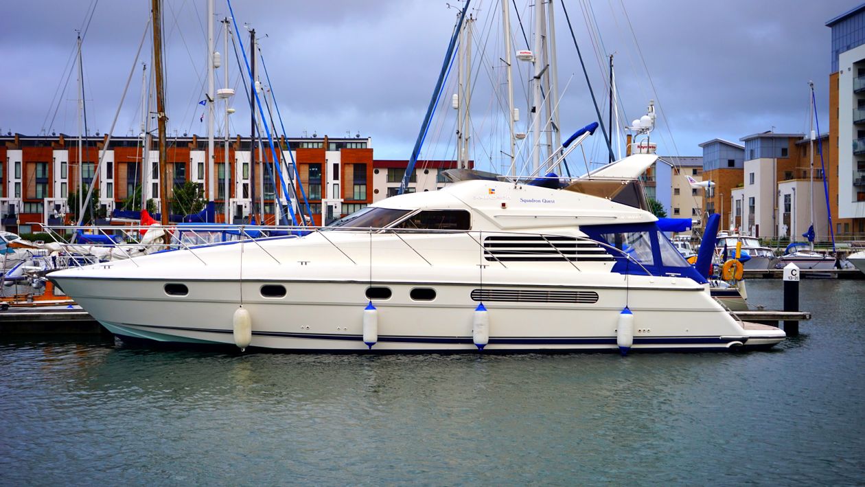 Hvid yacht fortøjet i marina med moderne bygninger i baggrunden